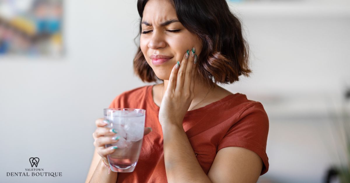 A person touches their cheek with a pained expression, indicating tooth sensitivity.