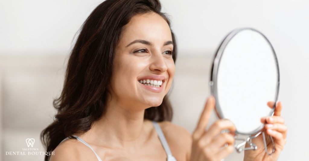 A person smiles at their reflection in the mirror, showing naturally white teeth.