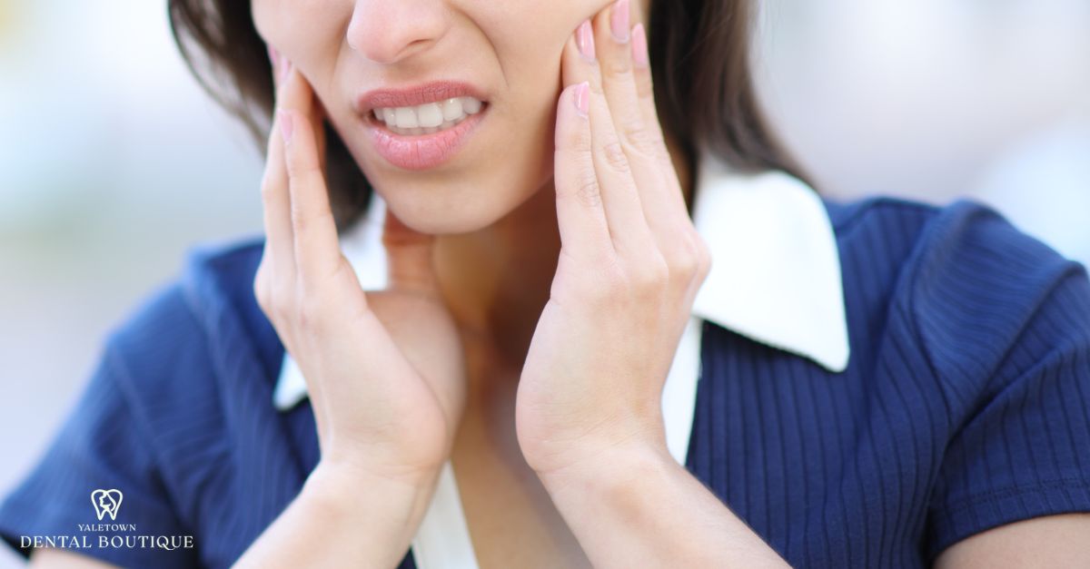 Woman holding her jaw in discomfort, illustrating common symptoms of TMJ disorder.