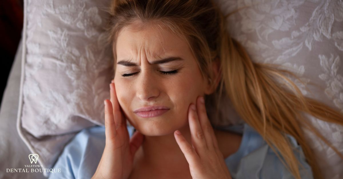 Close-up of a woman with pain linked to causes of jaw clicking, pressing her jaw area with visible tension