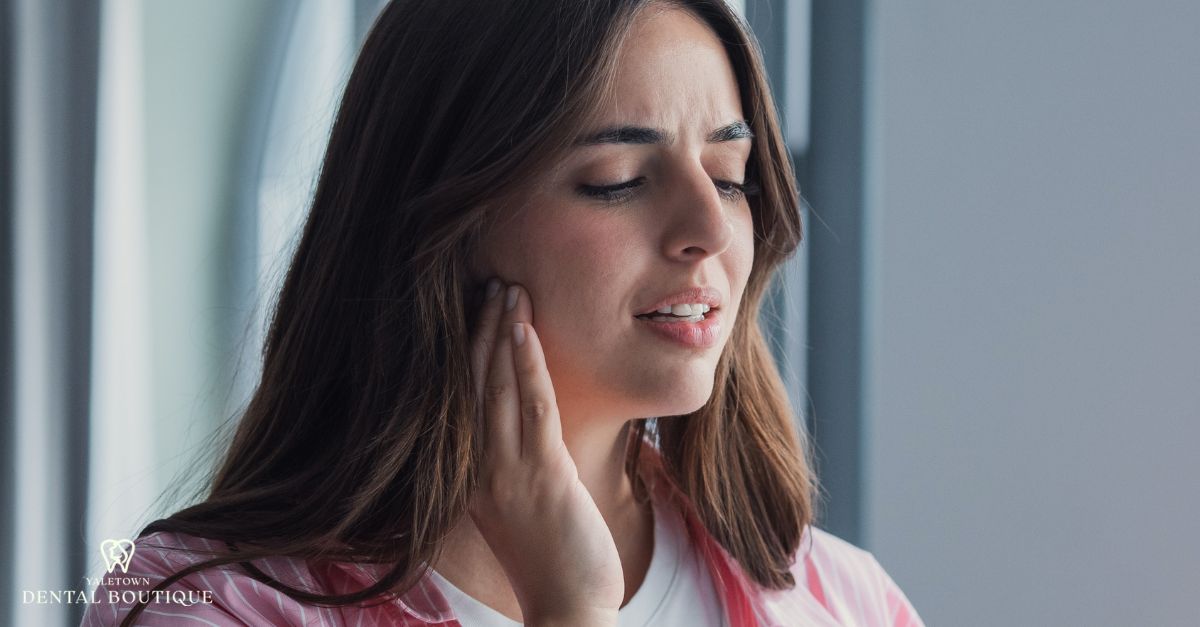 Close-up of a woman with jaw clicking, holding her jaw area as she feels tension near the joint